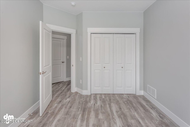 unfurnished bedroom with baseboards, visible vents, wood finished floors, and a closet