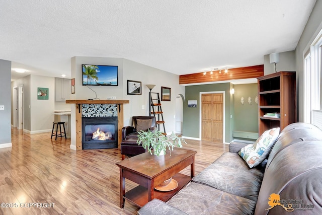 living room featuring light wood-style floors, baseboards, a tiled fireplace, and a textured ceiling