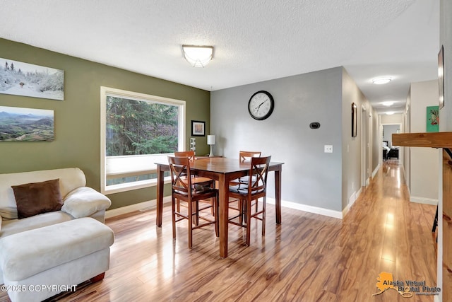 dining space with light wood-type flooring, a textured ceiling, and baseboards