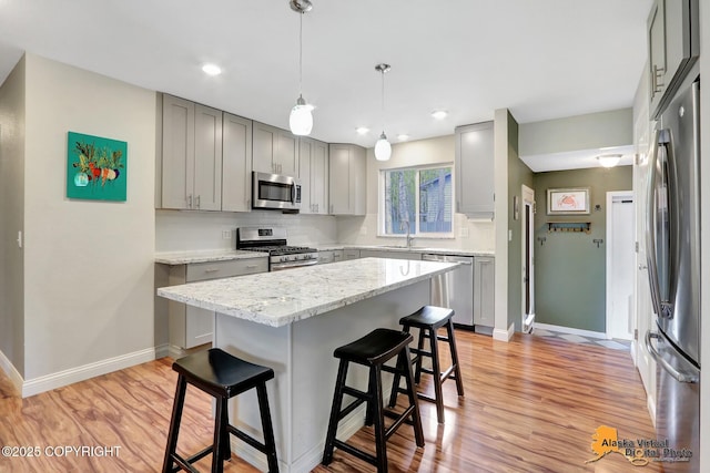 kitchen with appliances with stainless steel finishes, gray cabinets, a sink, a breakfast bar area, and baseboards