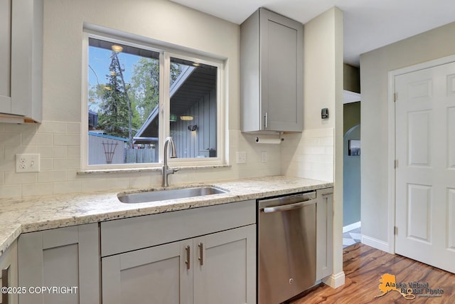 kitchen with stainless steel dishwasher, a sink, backsplash, light wood-style floors, and light stone countertops