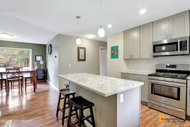 kitchen featuring stainless steel appliances, gray cabinets, light wood-style flooring, a center island, and a breakfast bar area
