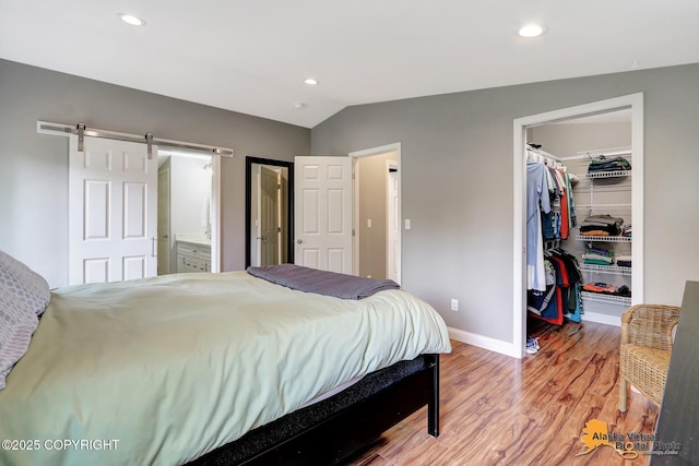 bedroom featuring a walk in closet, light wood-style flooring, baseboards, a closet, and vaulted ceiling