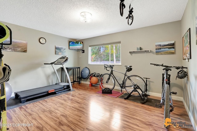 workout area with wood finished floors, a textured ceiling, and baseboards