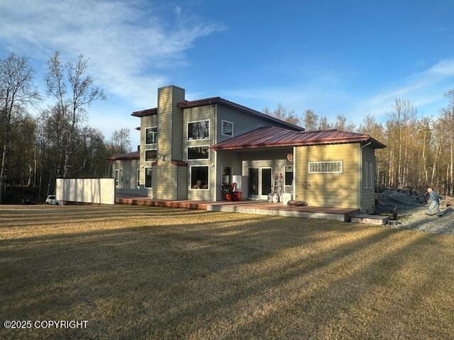 rear view of property featuring metal roof, a chimney, and a lawn