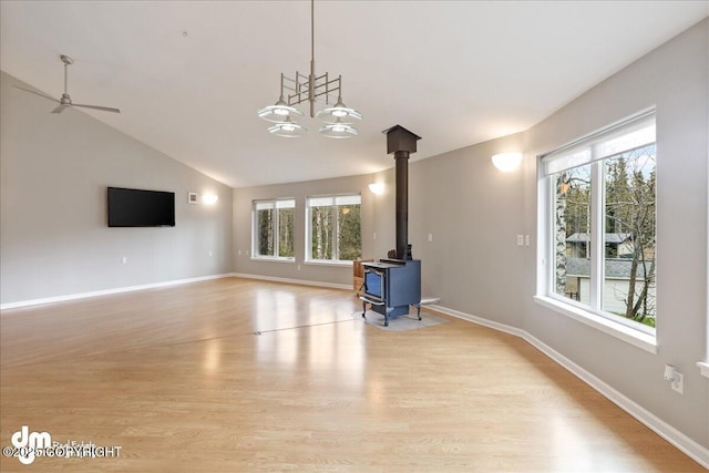 unfurnished living room with healthy amount of natural light, light wood-style floors, vaulted ceiling, and a wood stove