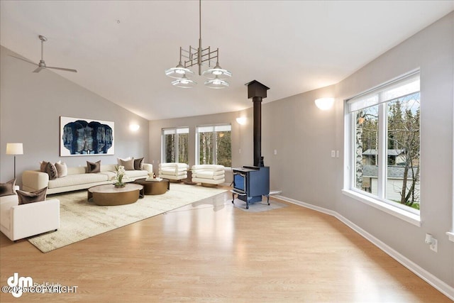 living room with a wood stove, wood finished floors, lofted ceiling, baseboards, and ceiling fan