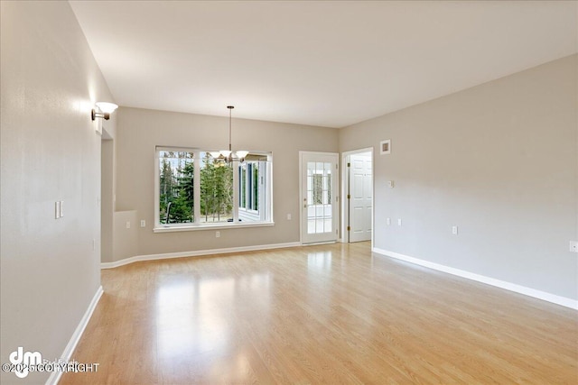 spare room featuring light wood-type flooring, a chandelier, and baseboards