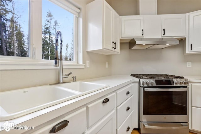 kitchen with stainless steel gas range, a sink, under cabinet range hood, white cabinetry, and light countertops