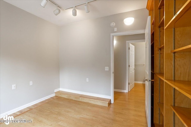 spare room with rail lighting, light wood-type flooring, and baseboards