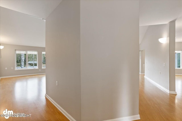 hallway with light wood-style floors, baseboards, and high vaulted ceiling