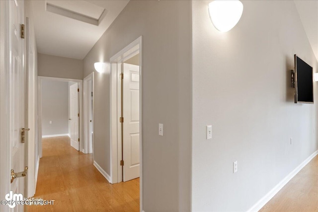 hall with light wood finished floors, attic access, and baseboards