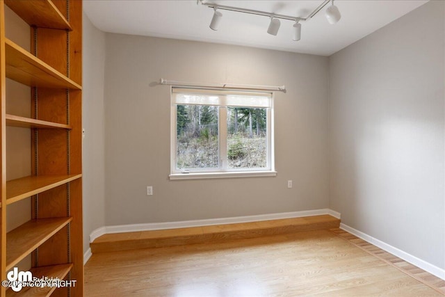 empty room with track lighting, light wood finished floors, and baseboards