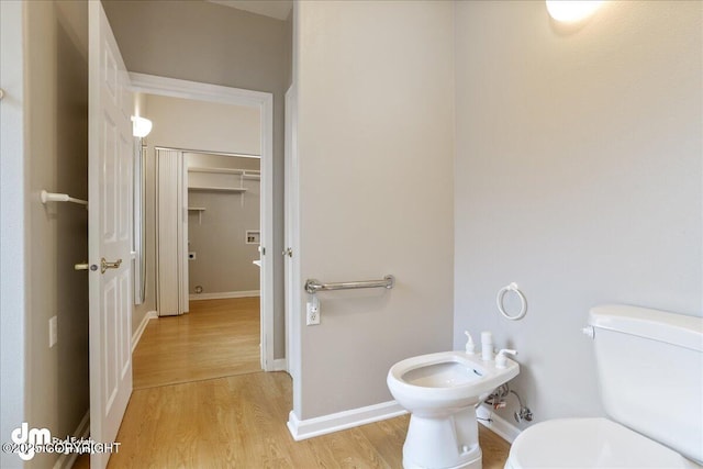 bathroom featuring toilet, wood finished floors, a bidet, and baseboards