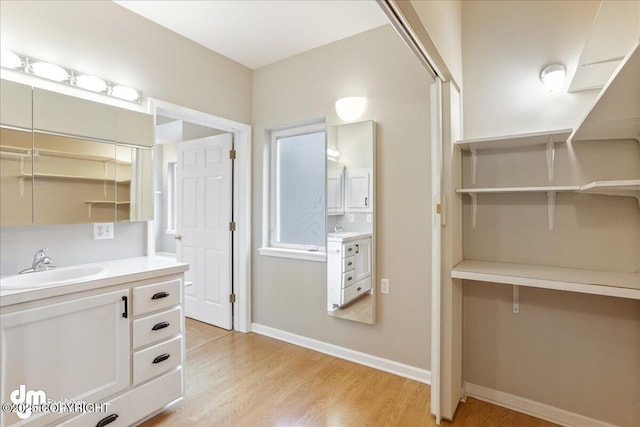 bathroom featuring wood finished floors, a walk in closet, vanity, and baseboards