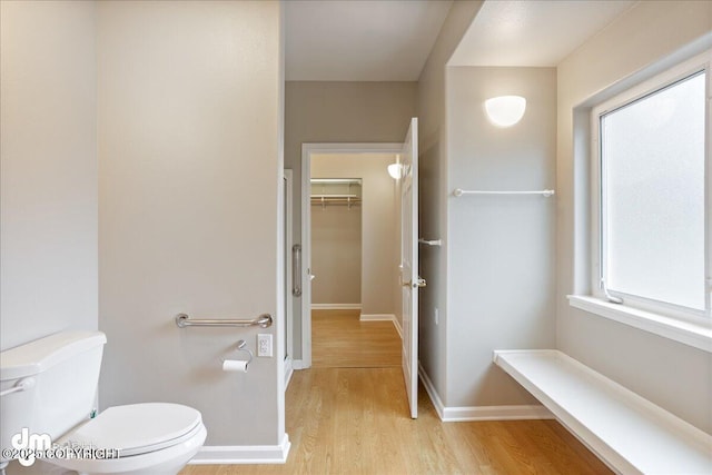 bathroom featuring wood finished floors, toilet, a walk in closet, and baseboards