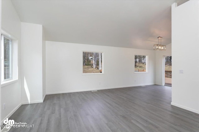 spare room featuring baseboards, wood finished floors, and a notable chandelier