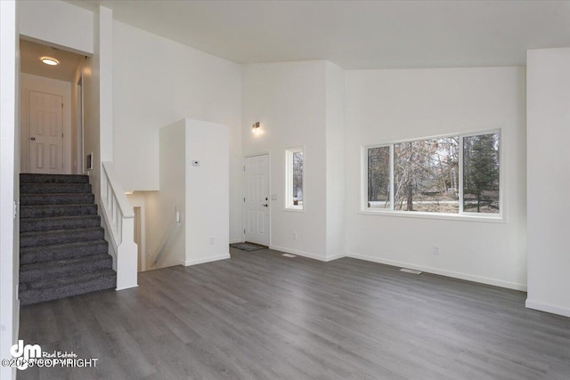 unfurnished living room featuring baseboards, stairs, and wood finished floors