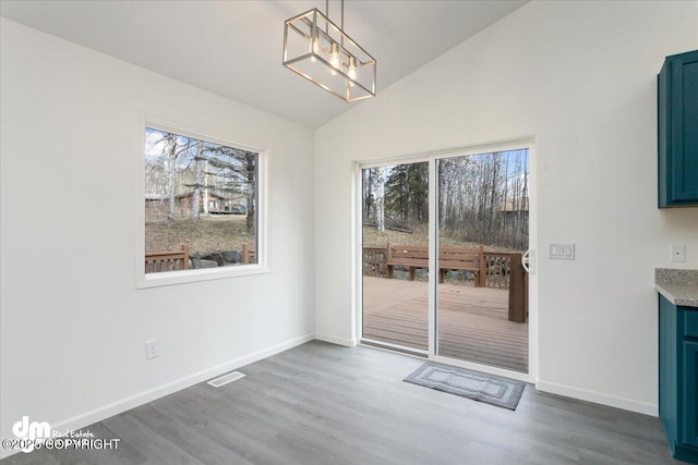 unfurnished dining area featuring visible vents, wood finished floors, baseboards, a notable chandelier, and lofted ceiling