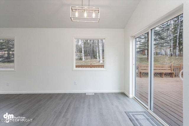 unfurnished dining area featuring baseboards, visible vents, wood finished floors, and lofted ceiling