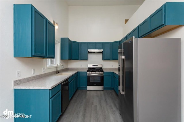 kitchen with a sink, appliances with stainless steel finishes, under cabinet range hood, and blue cabinetry