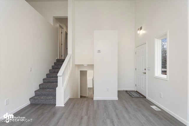 foyer entrance with baseboards, a towering ceiling, wood finished floors, and stairway