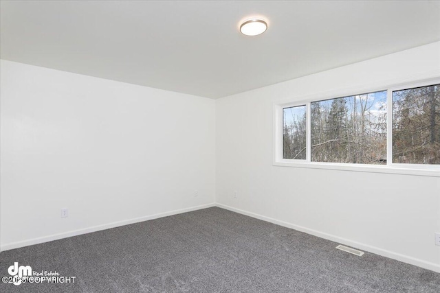 unfurnished room with visible vents, baseboards, and dark carpet