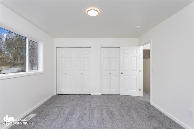 unfurnished bedroom featuring carpet flooring, baseboards, multiple closets, and visible vents