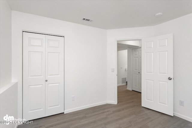unfurnished bedroom with baseboards, visible vents, wood finished floors, and a closet