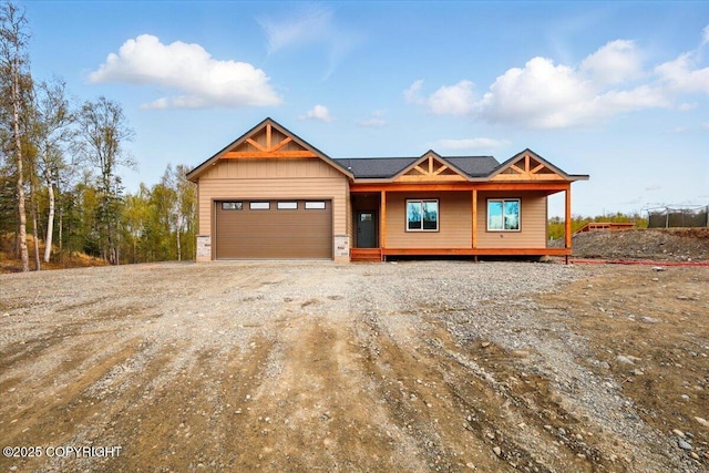 view of front of house with dirt driveway, an attached garage, and covered porch