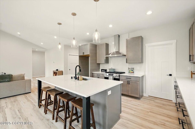 kitchen featuring wall chimney range hood, a sink, light wood finished floors, gray cabinets, and gas range