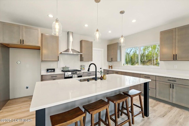 kitchen featuring a breakfast bar, wall chimney range hood, light countertops, stainless steel range with gas stovetop, and light wood-style flooring
