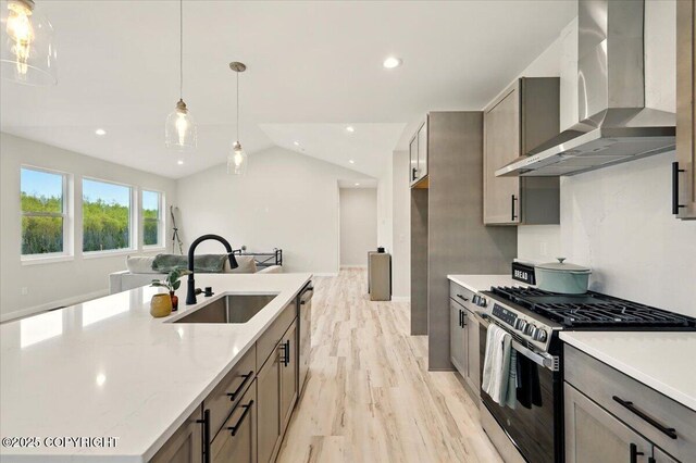 kitchen with wall chimney range hood, gray cabinetry, a sink, light wood finished floors, and stainless steel appliances