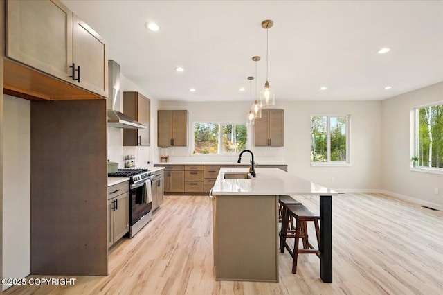 kitchen featuring wall chimney range hood, recessed lighting, a sink, light wood finished floors, and gas stove