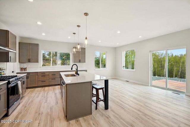 kitchen with a sink, light wood-style floors, light countertops, a kitchen island with sink, and stainless steel range with gas cooktop