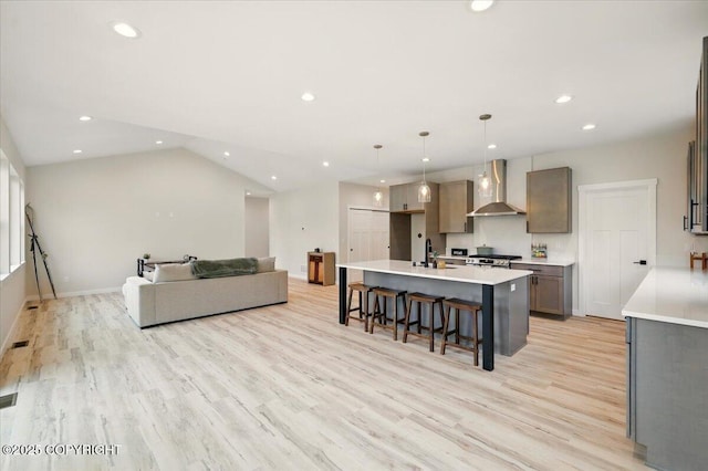 kitchen with light wood-style flooring, a kitchen island with sink, a sink, and wall chimney exhaust hood