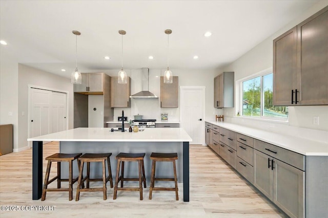kitchen featuring wall chimney range hood, a kitchen bar, and light wood-style flooring