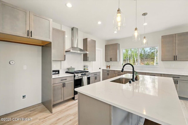 kitchen with stainless steel gas range, recessed lighting, wall chimney exhaust hood, a sink, and light wood-style flooring