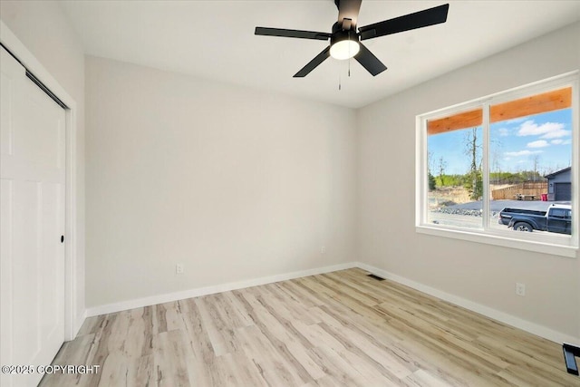 empty room with baseboards, ceiling fan, wood finished floors, and visible vents