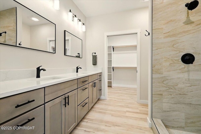 full bathroom with a sink, a tile shower, and wood finished floors