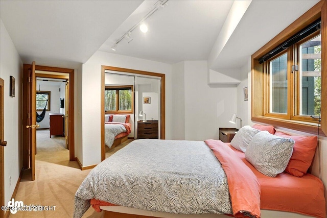 bedroom featuring light colored carpet, rail lighting, a closet, and baseboards