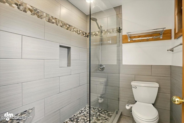 bathroom with toilet, a tile shower, and tile walls