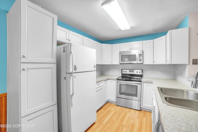 8515 Jewel Lake Rd # 25, Anchorage, AK 99502 - kitchen featuring appliances with stainless steel finishes, a sink, light countertops, light wood-style floors, and white cabinets