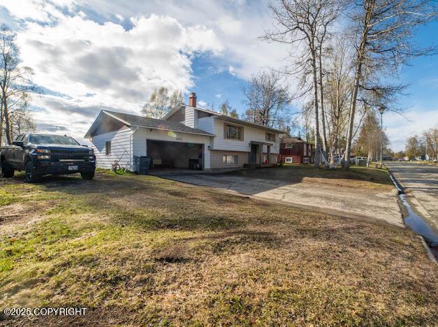 view of side of home with a chimney, driveway, a garage, and a lawn