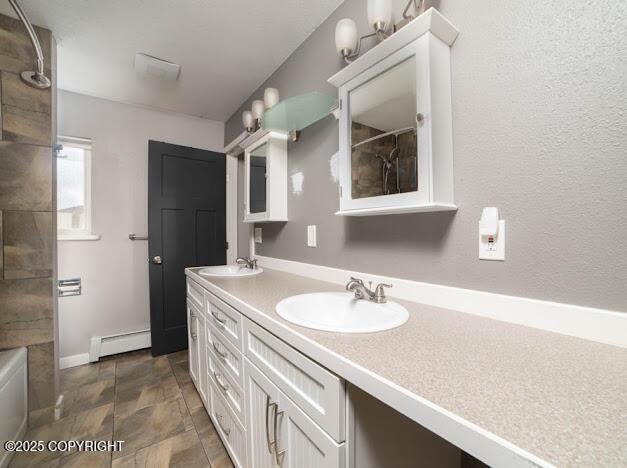 bathroom featuring baseboard heating, double vanity, stone finish flooring, and baseboards