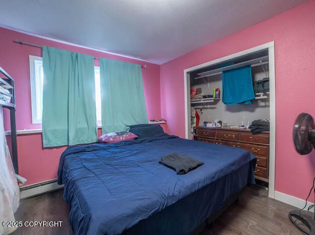 bedroom featuring a baseboard heating unit, wood finished floors, and baseboards