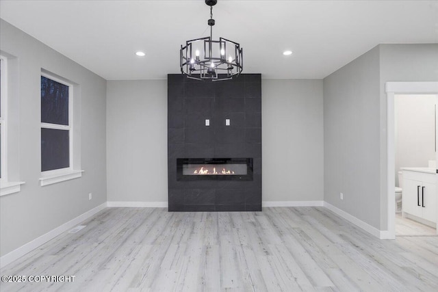 unfurnished living room featuring a chandelier, wood finished floors, baseboards, a large fireplace, and recessed lighting