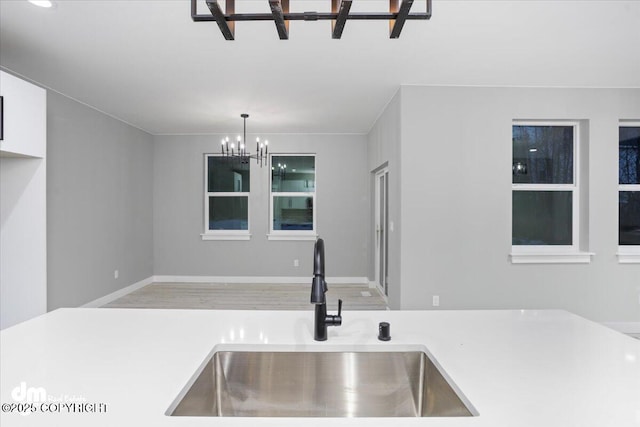 kitchen featuring a sink, a chandelier, wood finished floors, light countertops, and pendant lighting