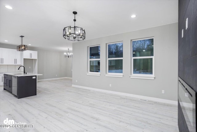 kitchen with a chandelier, a sink, light countertops, white cabinetry, and light wood-style flooring
