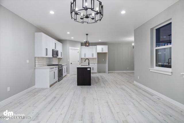 kitchen with appliances with stainless steel finishes, a kitchen island with sink, tasteful backsplash, a sink, and a chandelier